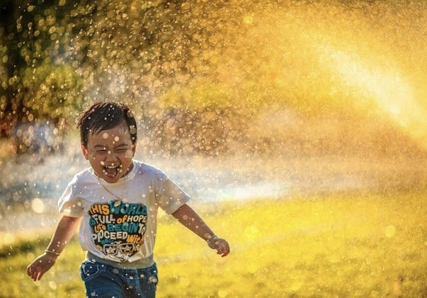 kid running in sprinkler with sunshine
